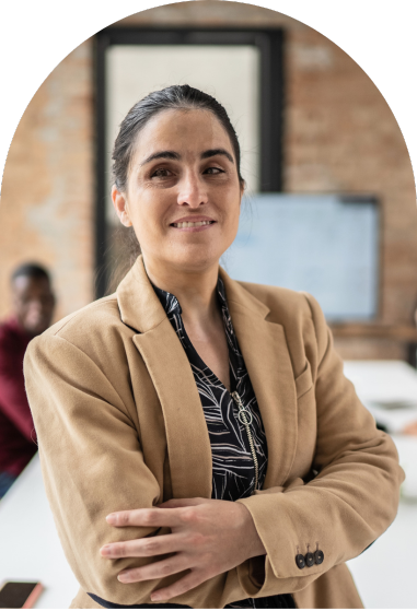 Accessibility training for employers. A smiling portrait of a woman wearing a beige blazer with a visual impairment. She appears to be in a work environment, which is blurred behind her.