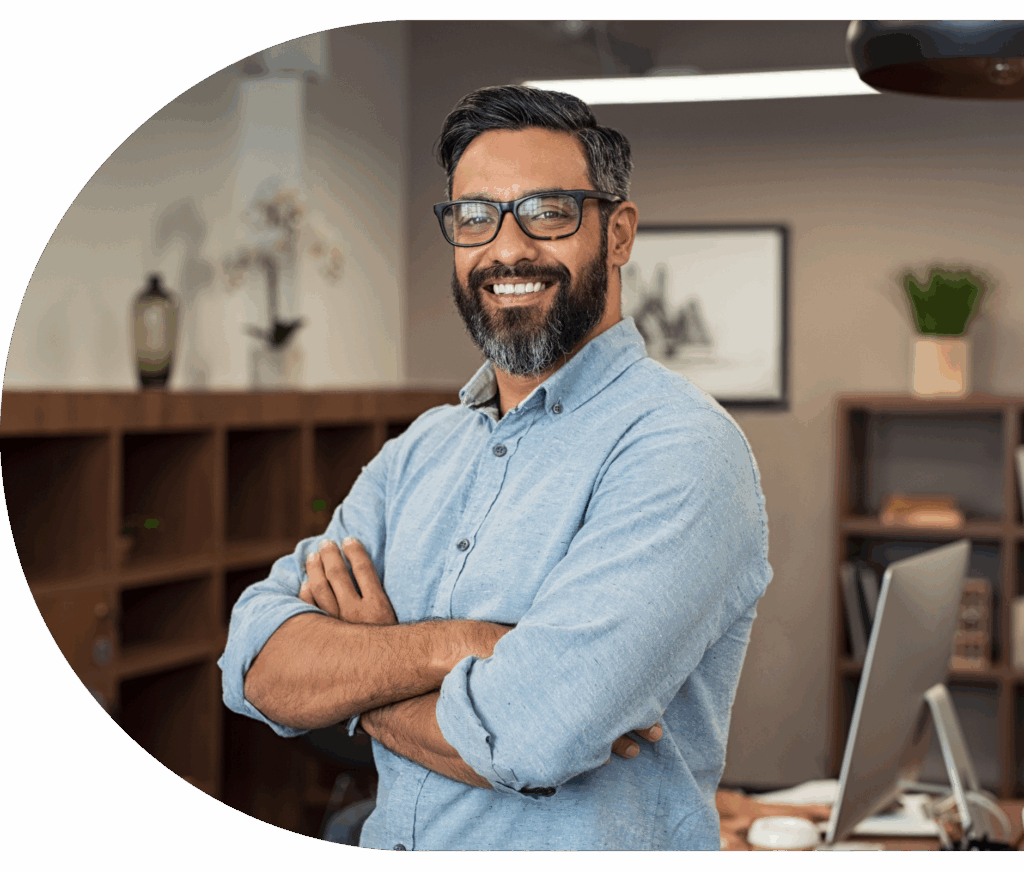 Secure your limited-time recruitment offer with Envol. Image includes a smiling man with dark hair and a dark beard looking at the camera crossing his arms. He is situated in an office which is blurred in the background. He wears a light blue button-down shirt.